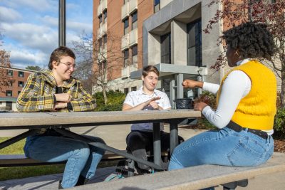 Students engage in a conversation using American Sign Language (ASL) while seated at an outdoor picnic table.