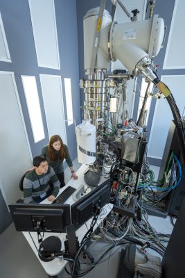 Two researchers are working with a large, complex piece of scientific equipment