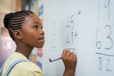 A young girl is deeply focused as she works on a math problem on a whiteboard.