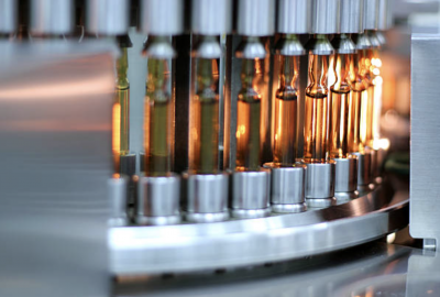 A close-up view of a pharmaceutical production line. Glass vials are being processed by automated machinery.