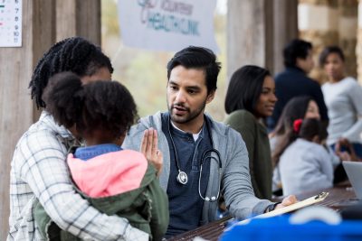 Volunteer eye doctor holds up three fingers while checking a little girl's vision. The girl and her mom are visiting a free clinic.