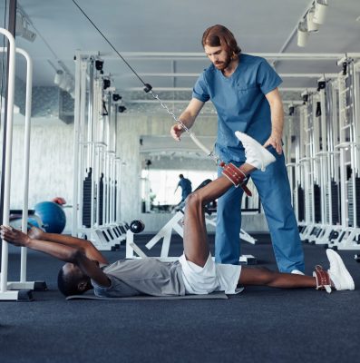 African patient doing physical exercises for recovery with the help of doctor in health club