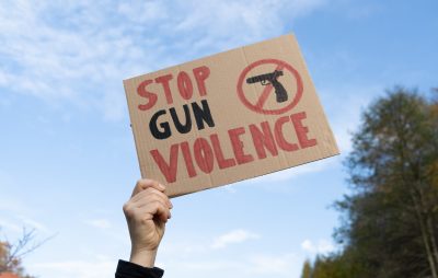 Hand holding a sign with slogan Stop Gun Violence and black pistol strikethrough. Woman with placard at protest rally demonstration strike to ban weapons and end shooting.