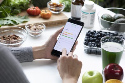 Woman Asian Professional Nutritionist busy working and checking data from a phone with a variety of fruits, nuts, vegetables, and dietary supplements on the table