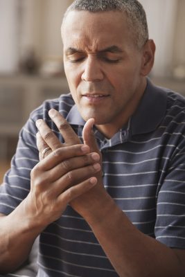 a mature man, likely experiencing discomfort or pain, as he grasps his hand with a look of discomfort on his face.