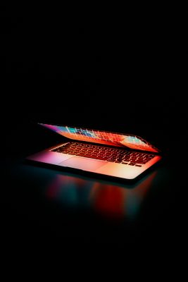 A partially open laptop sits on a dark surface, illuminated by the vibrant, multicolored glow from its screen and keyboard.