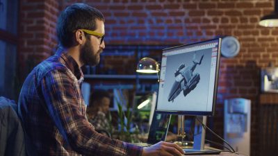 A man works on a 3D model of a futuristic vehicle displayed on a computer screen.