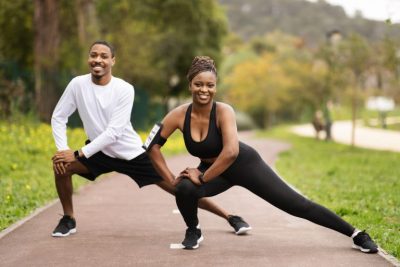 A man and a woman exercising outdoors, both engaged in a stretching routine.