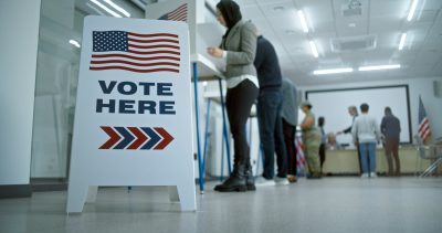 Vote here sign on the floor. Multi ethnic American citizens vote in booths in polling station office. National Election Day in United States. Political races of US presidential candidates. Civic duty.