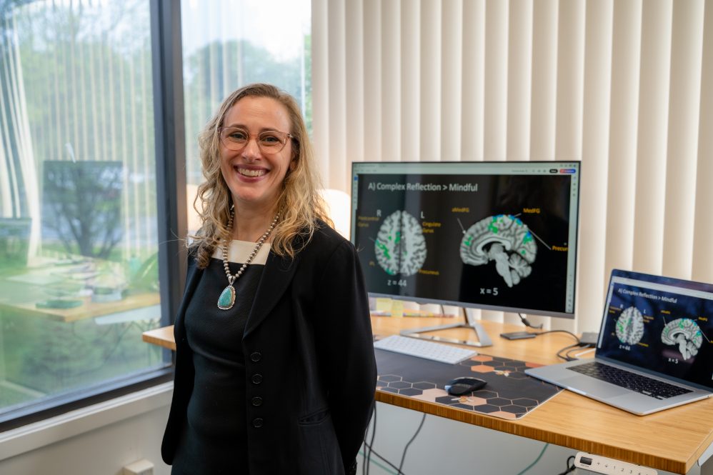 Sarah Feldstein Ewing, Ph.D. standing next to computer showing brain diagram